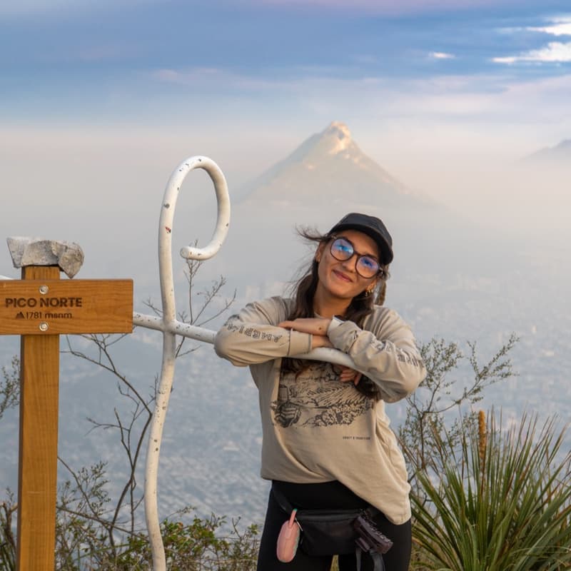 Excursionista junto al letrero de la cumbre del Pico Norte, con Monterrey al fondo